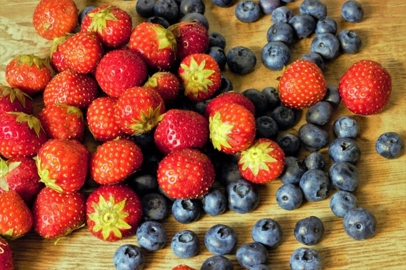 Fotografía en primer plano de frutos rojos, fresas y arándanos, sobre una mesa de madera. / Fuente: Pixabay/András.